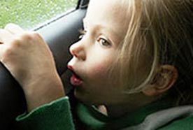 A young girl sitting in a car looking out the window at the rain